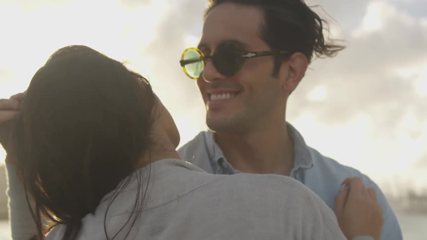 A man and woman smile and hug on a windy day