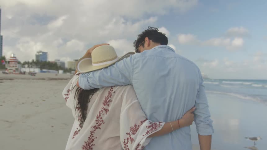 Man and woman walk on the beach with the arms around each other