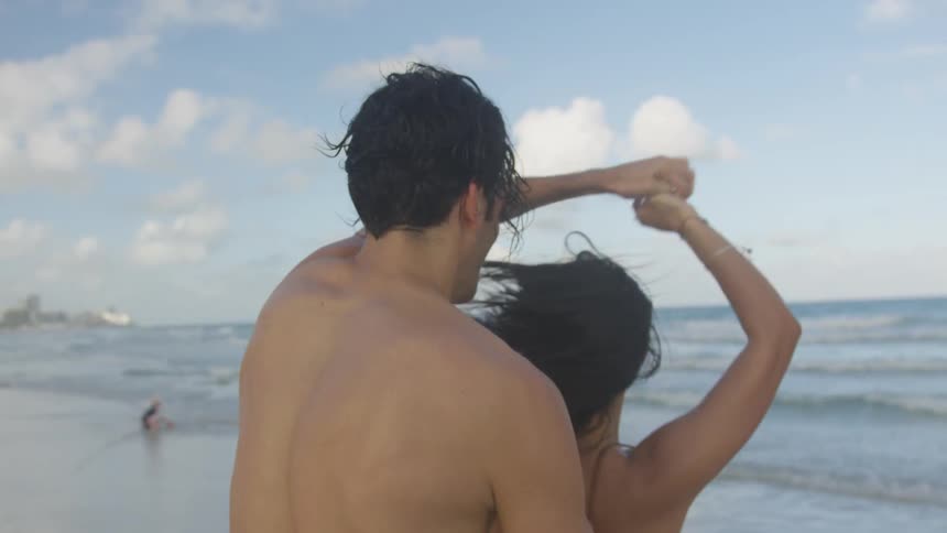 A man laughs as he twirls and dances with a woman on the beach
