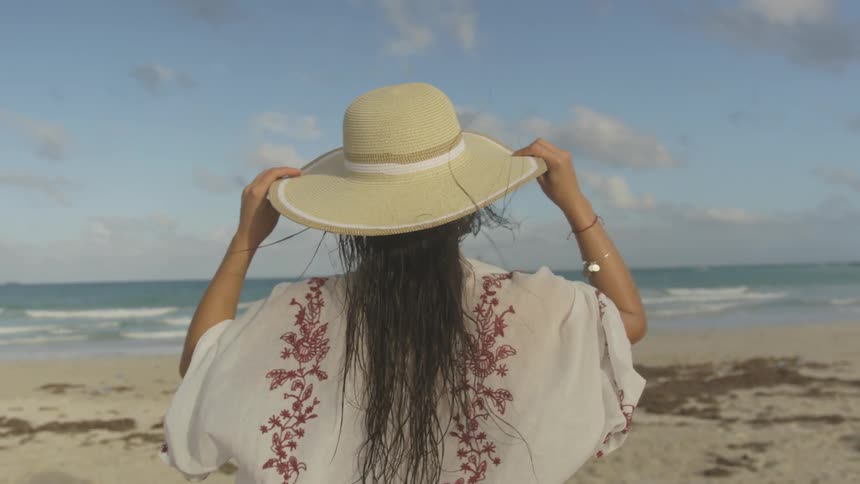 Woman walks on the beach holding her hat