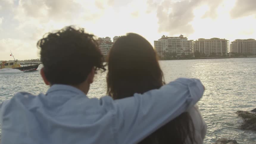 The man has his arm over the woman's shoulder as the boat passes