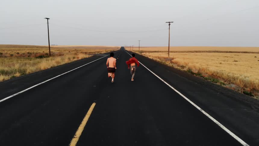 Two men run down a long road in a rural area at day time