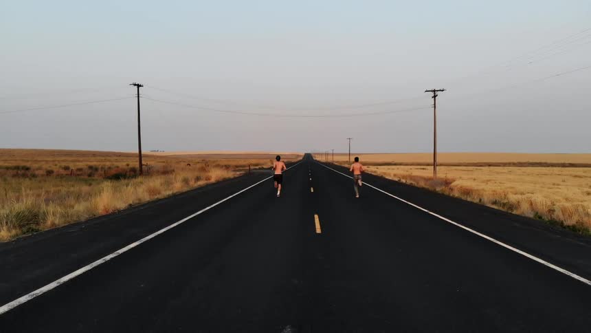 Two boys are running down the middle of a rural road in daylight