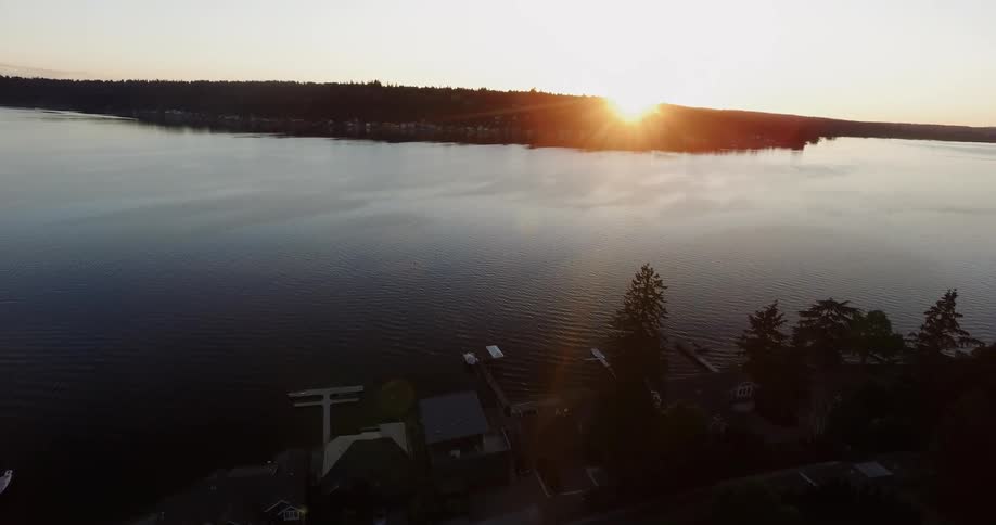 A body of water surrounded by land with the sun setting in the distance