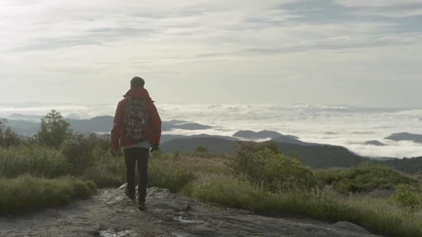 A man carrying a camera walks to the edge of a ridge