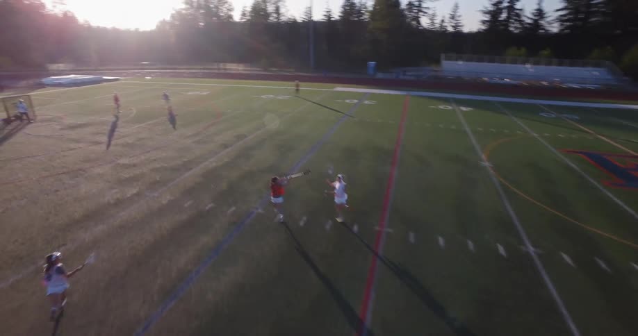 Women playing lacrosse on a field on a sunny day