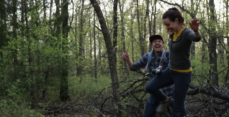 A man helps a woman walk over a large tree log