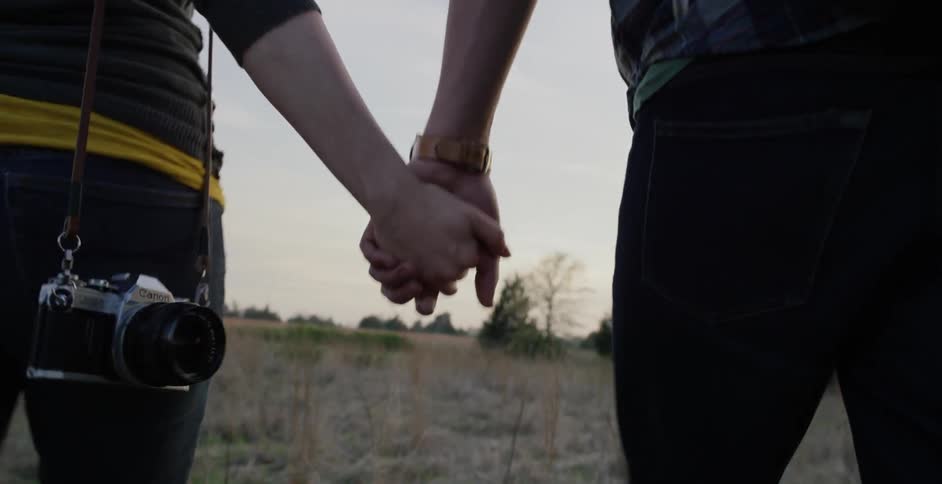 Man and woman holding hands and walking through a field