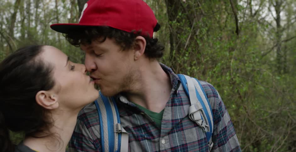 A man and women look at the forest then turn to each other for a kiss
