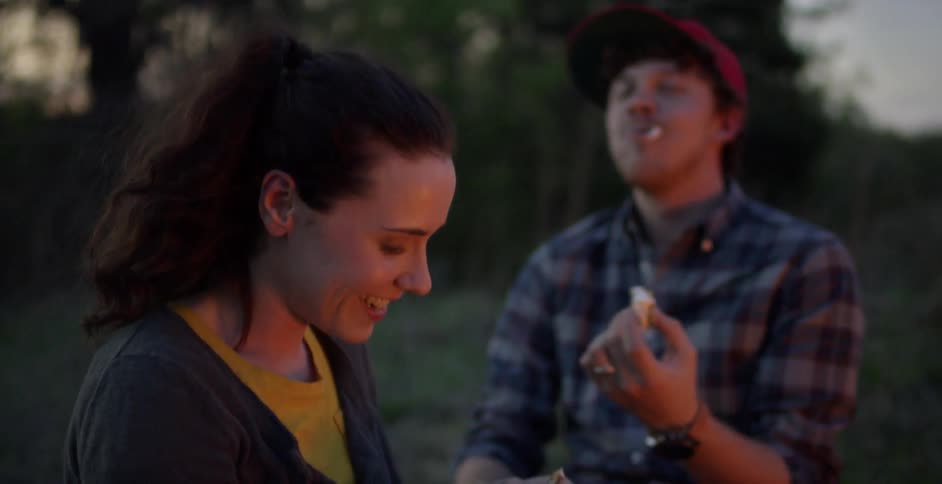 A woman feeds a s'more to a man at dusk
