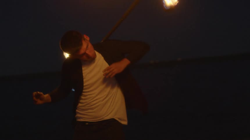 Man spins sticks of fire around his body outside at night