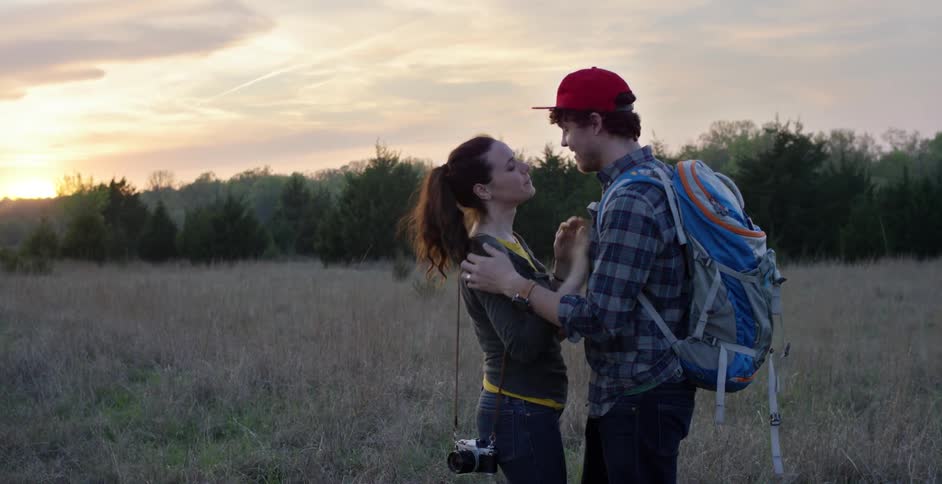 A man and woman embrace at dusk on a large field
