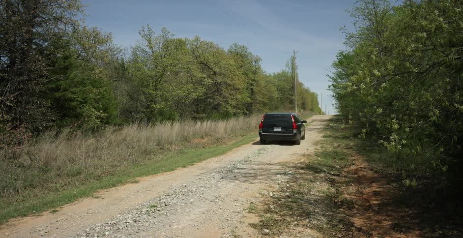 A station wagon is traveling down a dirt road