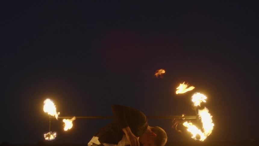 A man twirls a flaming baton at night