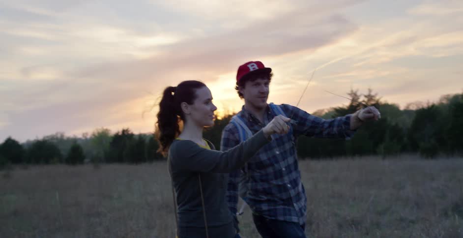 Man and woman walking through a field, waving sticks
