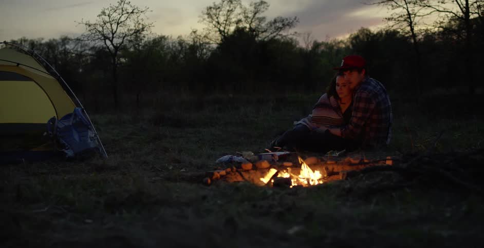 A man and woman cuddle next to a campfire