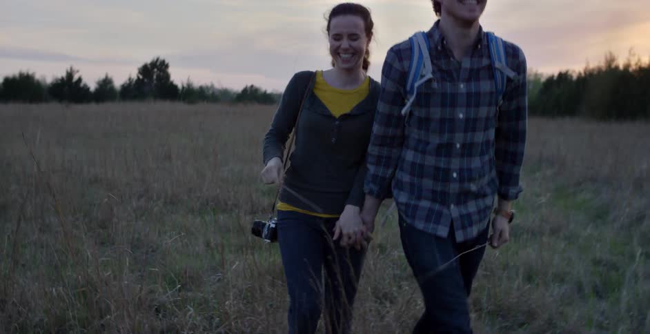 A man and woman are holding hands as they walk through a field