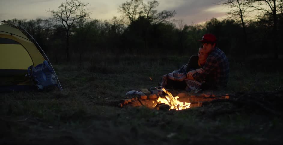 Two people cuddling by a campfire at dusk