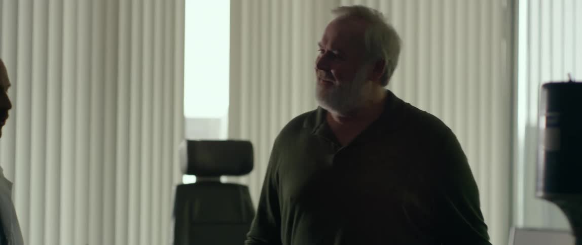 A man walks into a room with a doctor and leans against the wall as the doctor talks