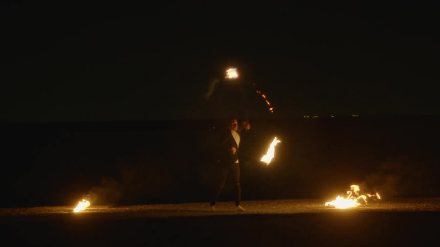 The man spins a staff with fire on each end at night