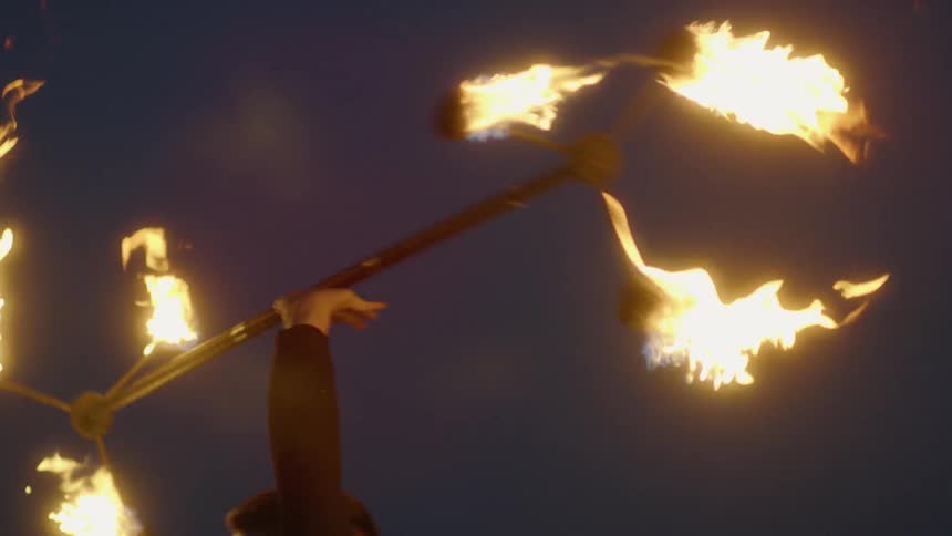 The man twirls the pole with fire at each end