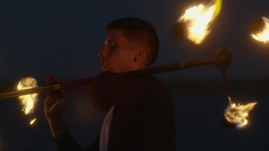 Man waves flaming fire sticks around his body outside at night
