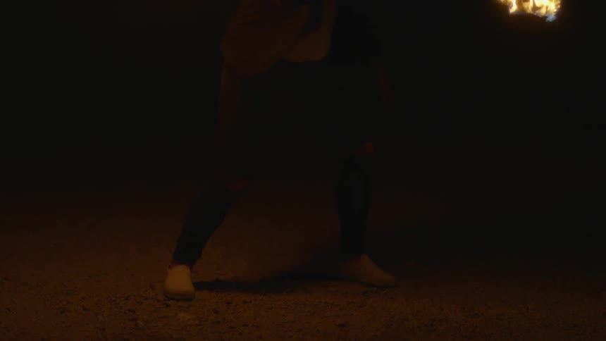 A person standing outside at night twirling a lit torch