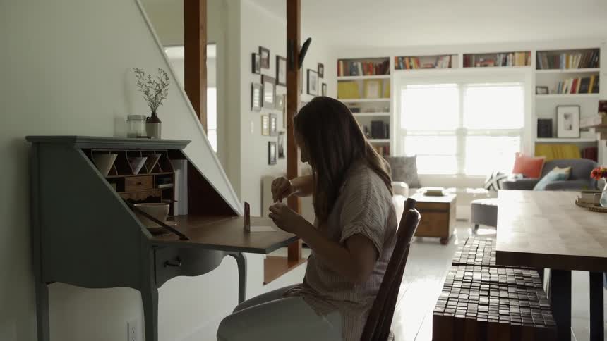 A woman sits at a desk and sharpens a pencil