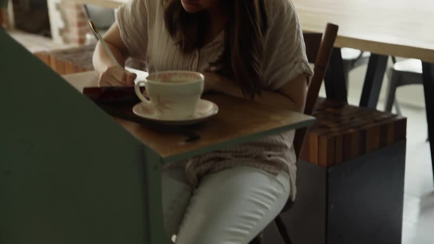 Woman sits at a table with a mug of coffee writing in a small book