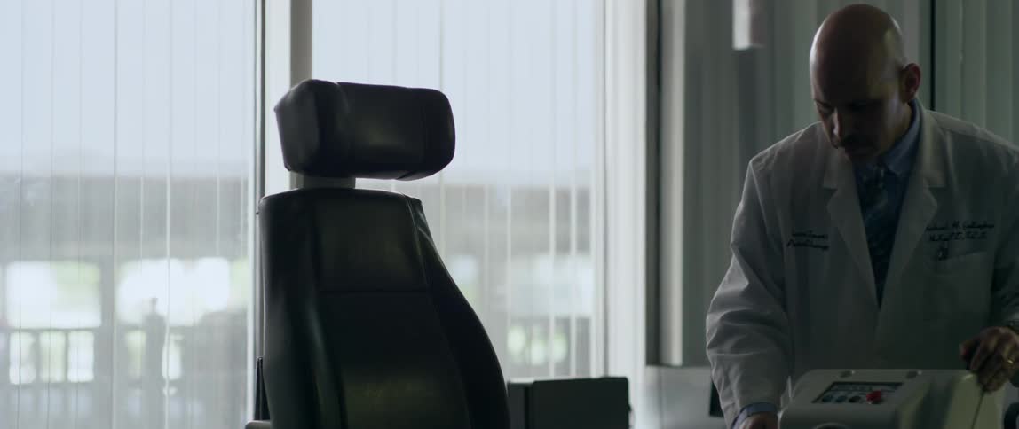 A doctor walks around a chair in an office