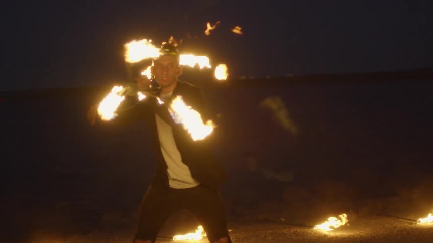 Man waves flaming fire sticks around his body