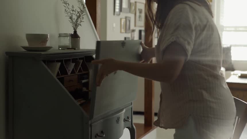 A woman pulls out a chair and opens the lid of a desk