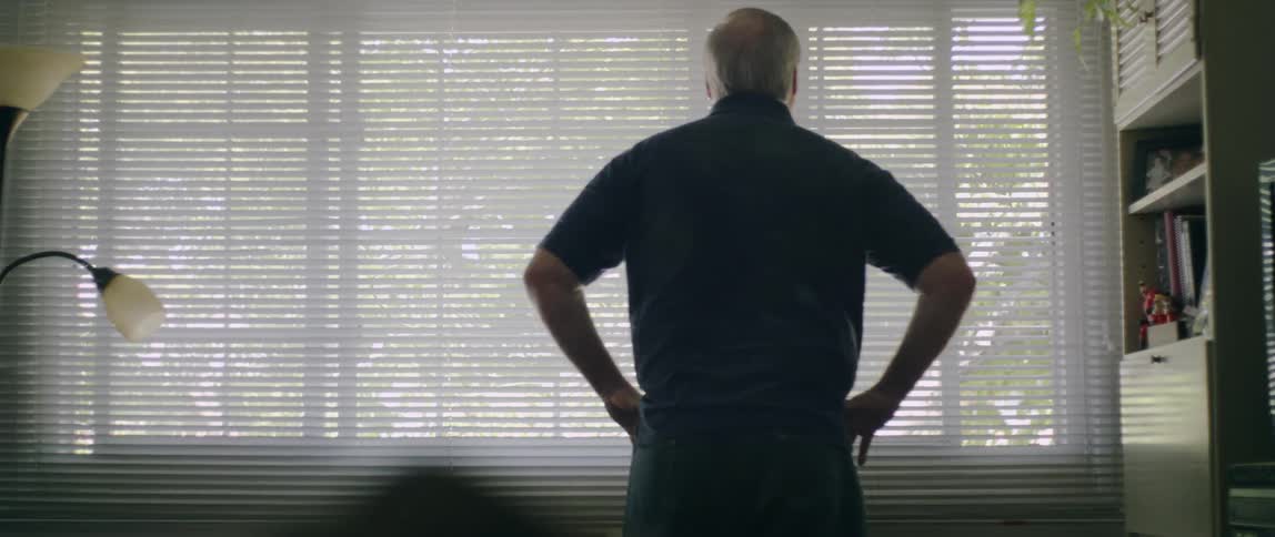 A man peeks through the blinds of a large window at day time