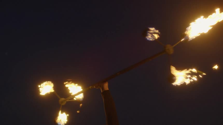 A man twirls a long flaming baton at night