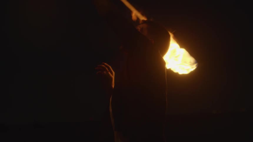 A man twirls a torch outside at night