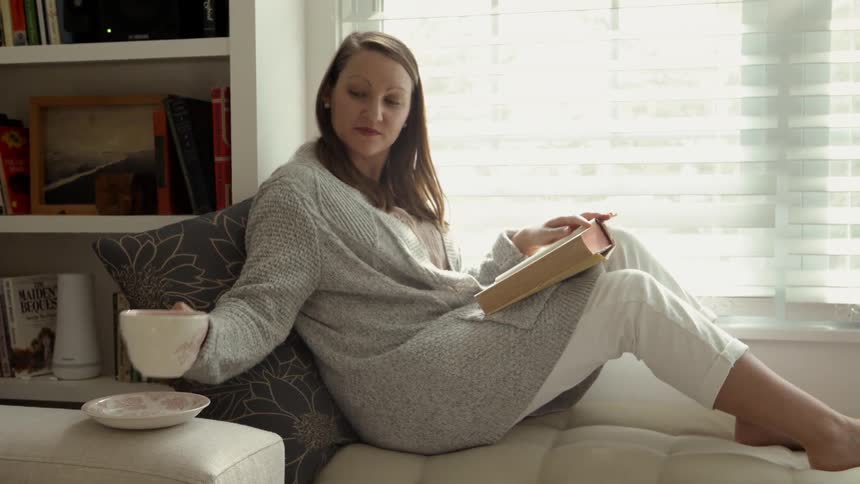 A woman sits drinking coffee and reading