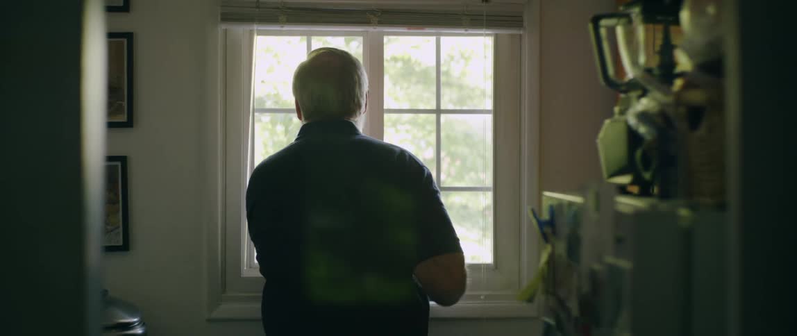 A man walks over to and looks out a window