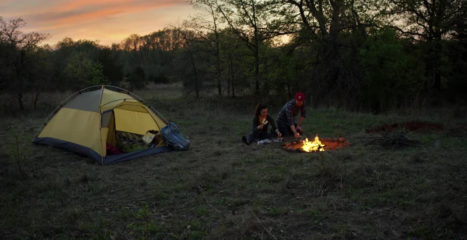 Couple camping and toasting marshmallows at sunset