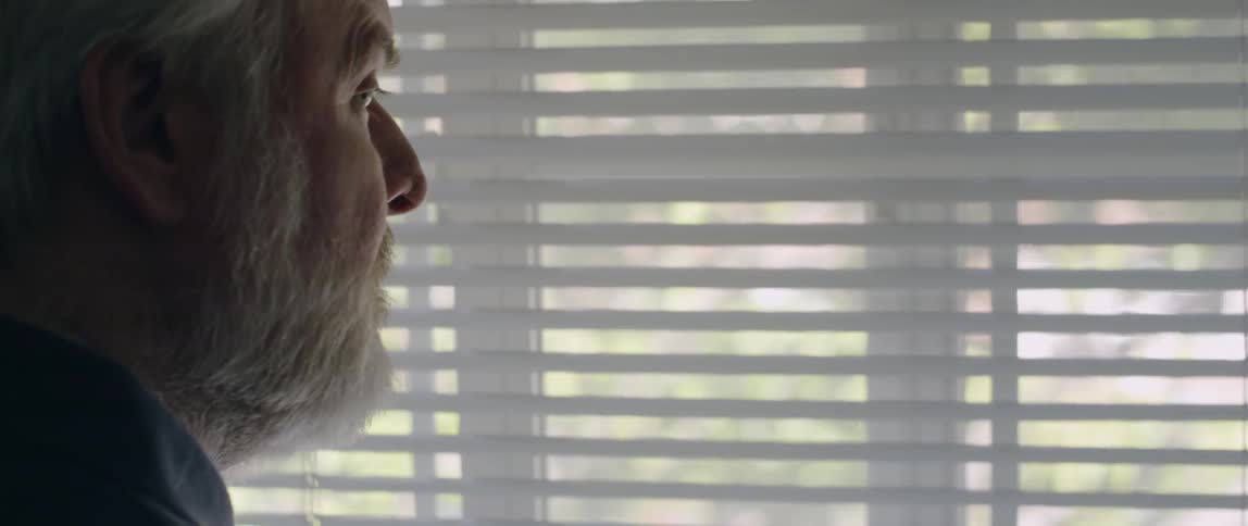 Man looks through the blinds then steps away