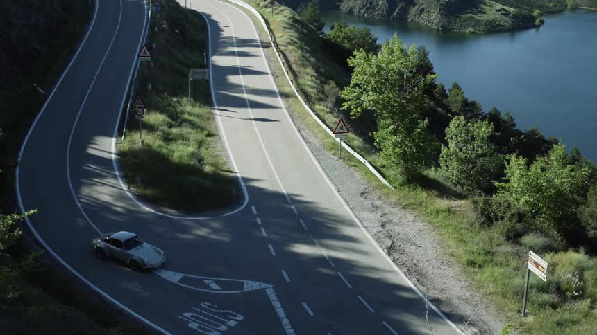 A retro-looking car turns in a sharp mountain curve