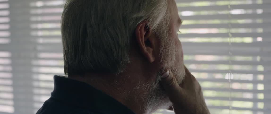 A man holds his chin while looking out a window