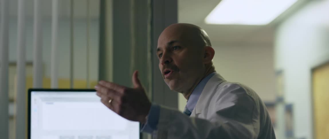 A man talks and gestures while looking at a monitor