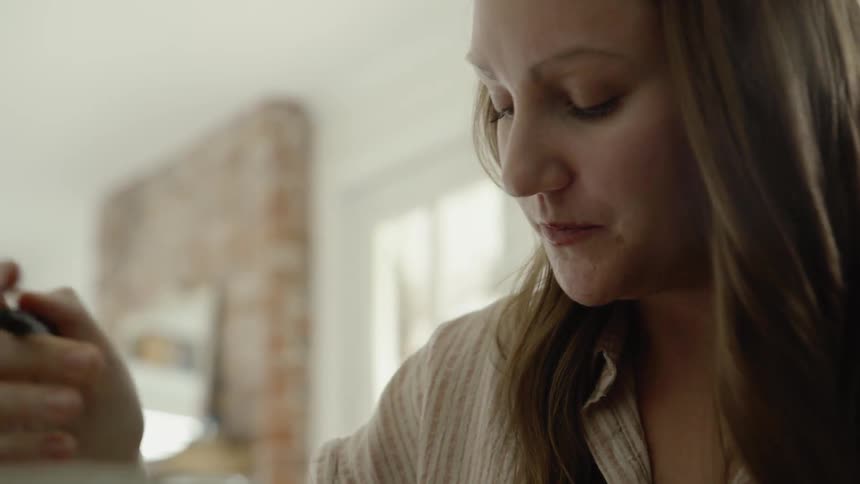 A woman drinks from her mug and begins writing