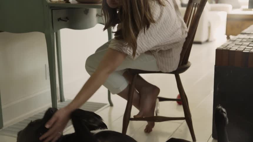 A woman leans down and pets her dog while sitting at a desk