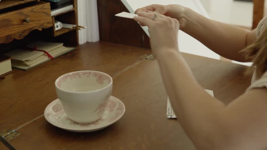 A woman places a stamp on a postcard and puts the other stamps away