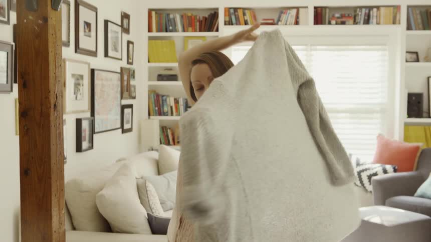 A woman takes a sweater off a coat rack and puts it on