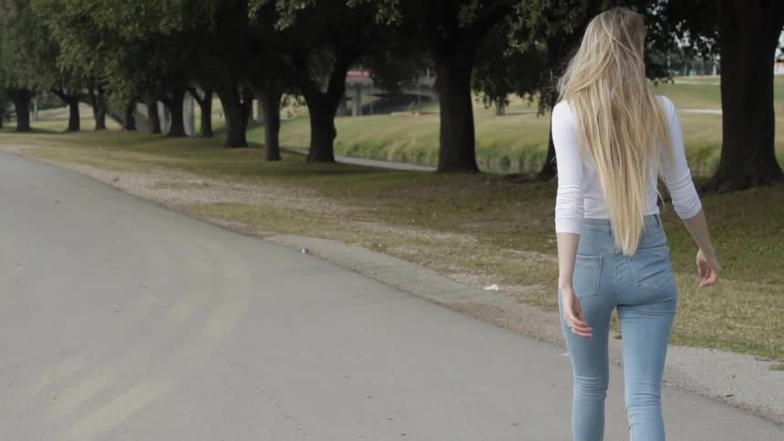 A woman walks down a tree lined road during the day