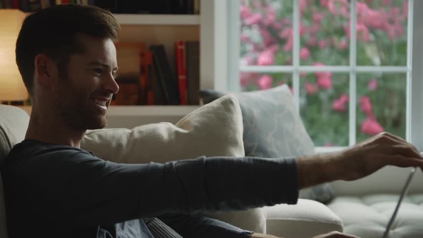 A man sitting on a couch looks at someone and laughs