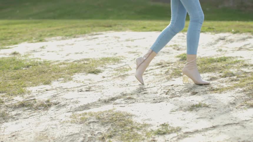 The woman walks on the grass with high heel boots