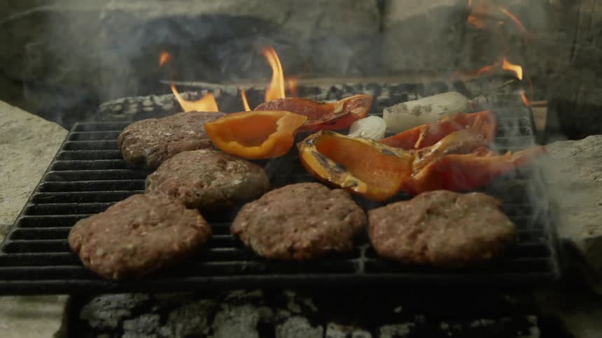 Meat and vegetables cook on the grill over a hot fire